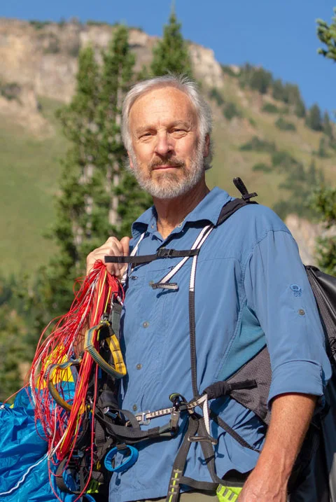 Dan Schilling in the mountains, carrying a paraglider rig